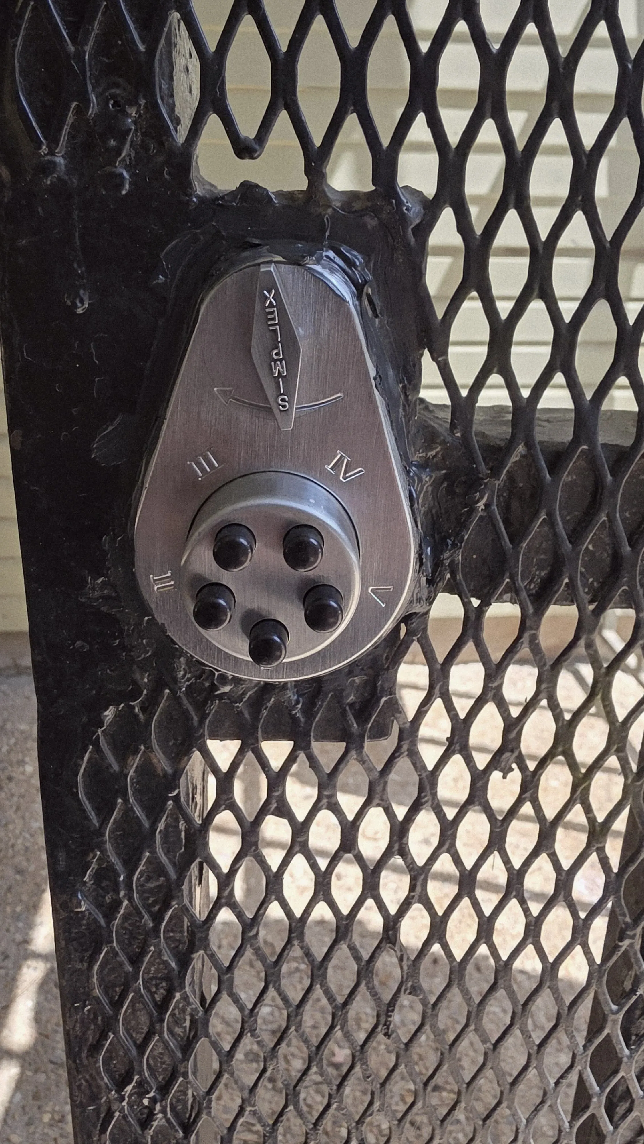 A Simplex pushbutton lock installed on an iron gate, an example of no-drilling-required access hardware