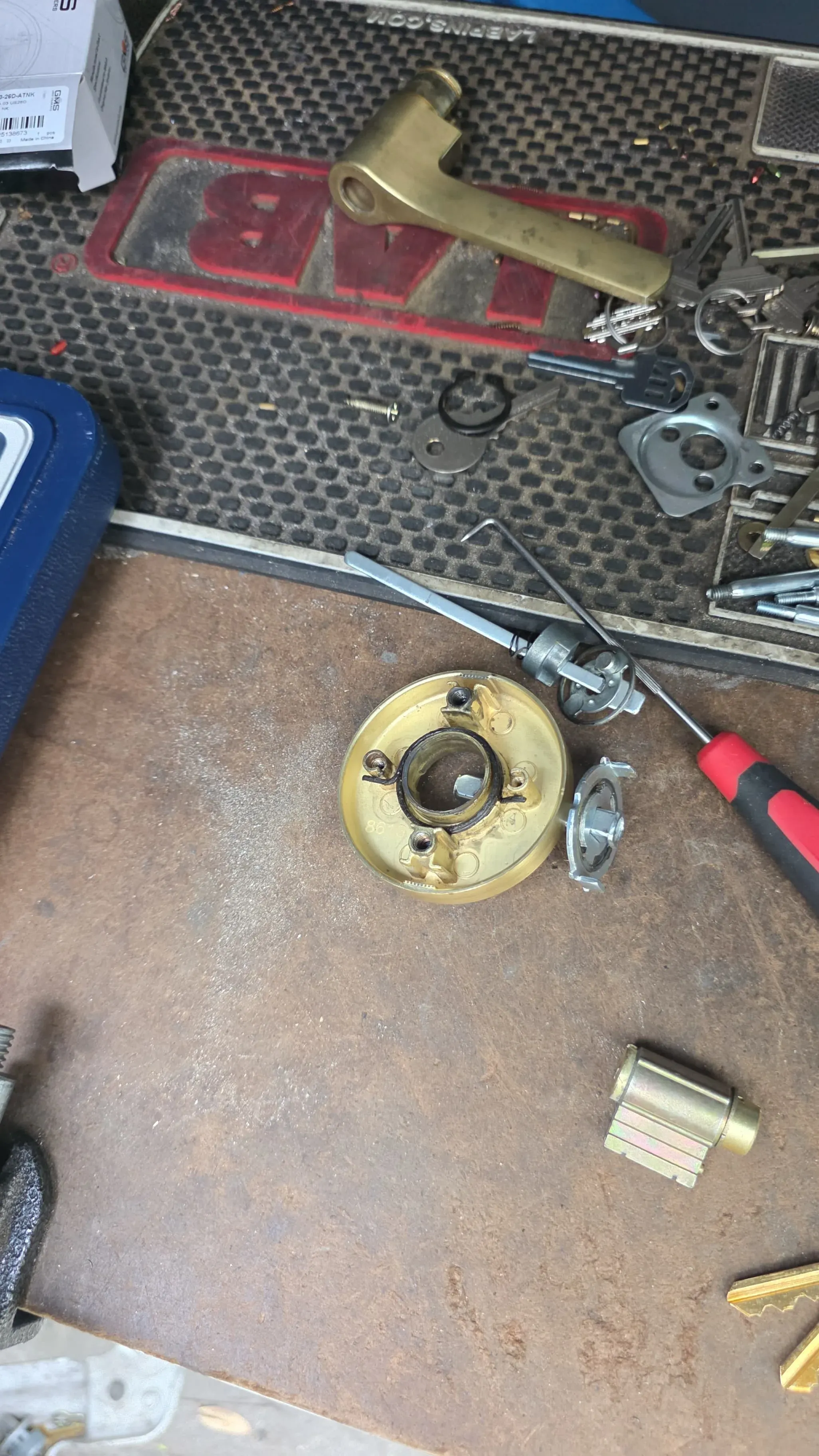 A disassembled lock cylinder and lever handle laid out on a workbench mat alongside picks and keys