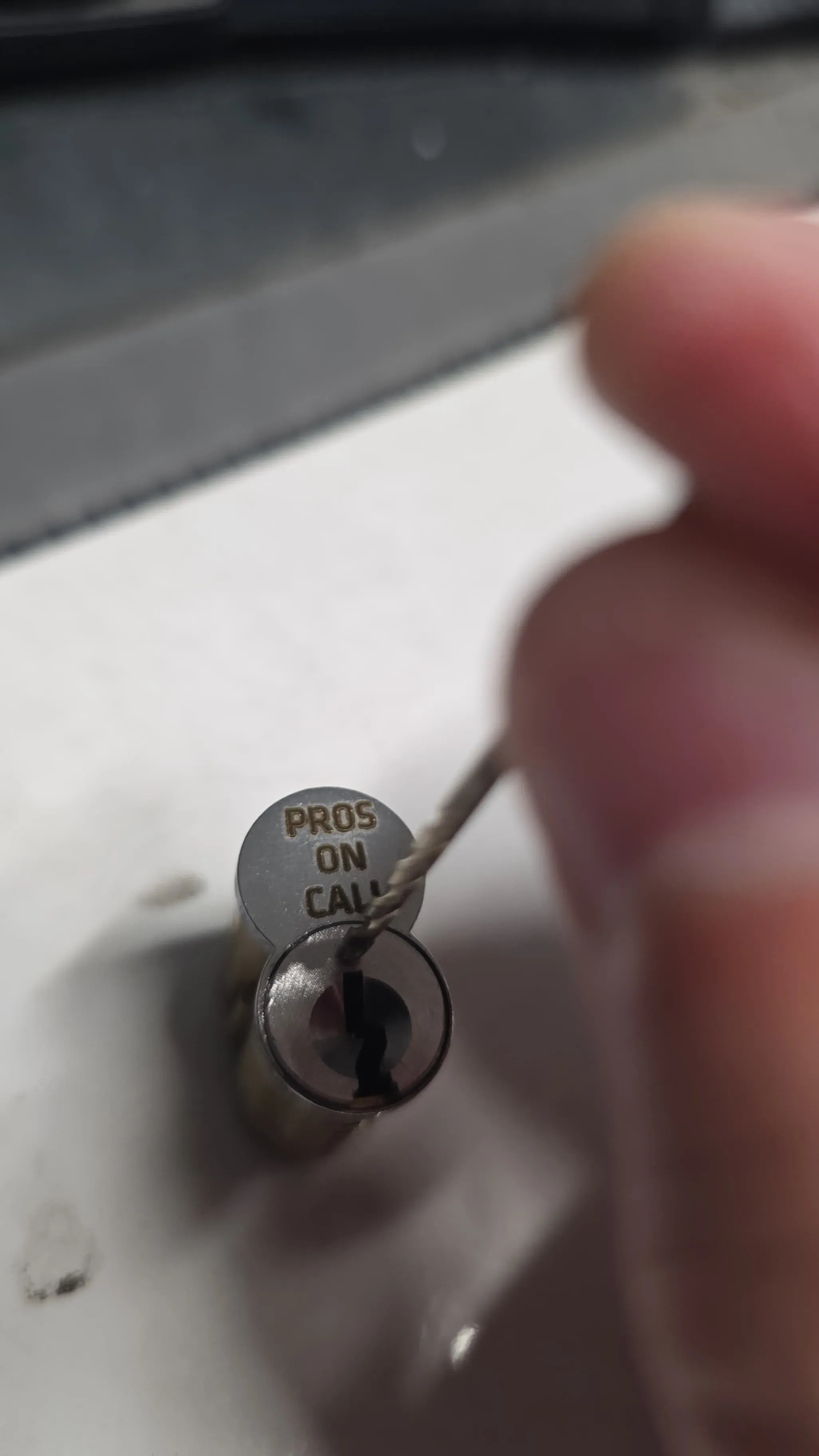 A Pros On Call branded lock cylinder with a rekeying tool inserted into the keyway