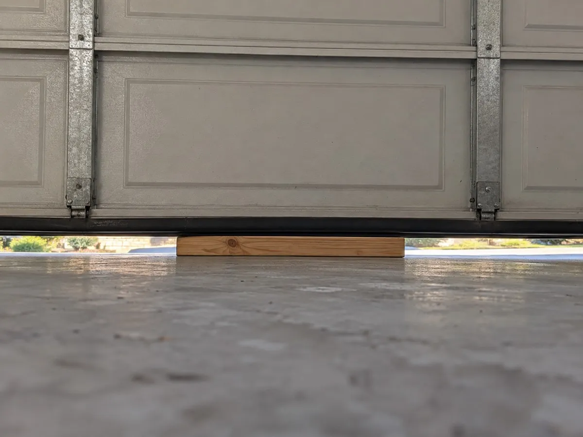 Garage door lowered onto a flat 2x4 board on a concrete floor for a monthly safety reversal test in Lockhart