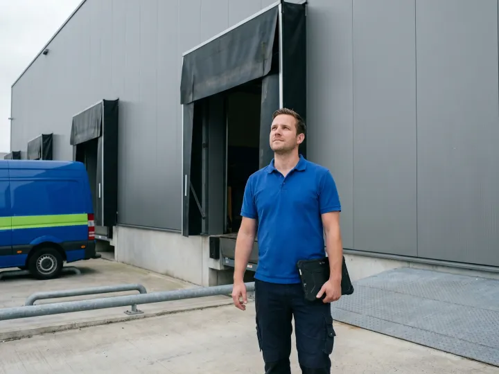 Pros On Call technician with tablet at commercial warehouse loading dock, cobalt blue and lime-green service van visible, high-speed fabric roll-up door partially open, Austin Texas