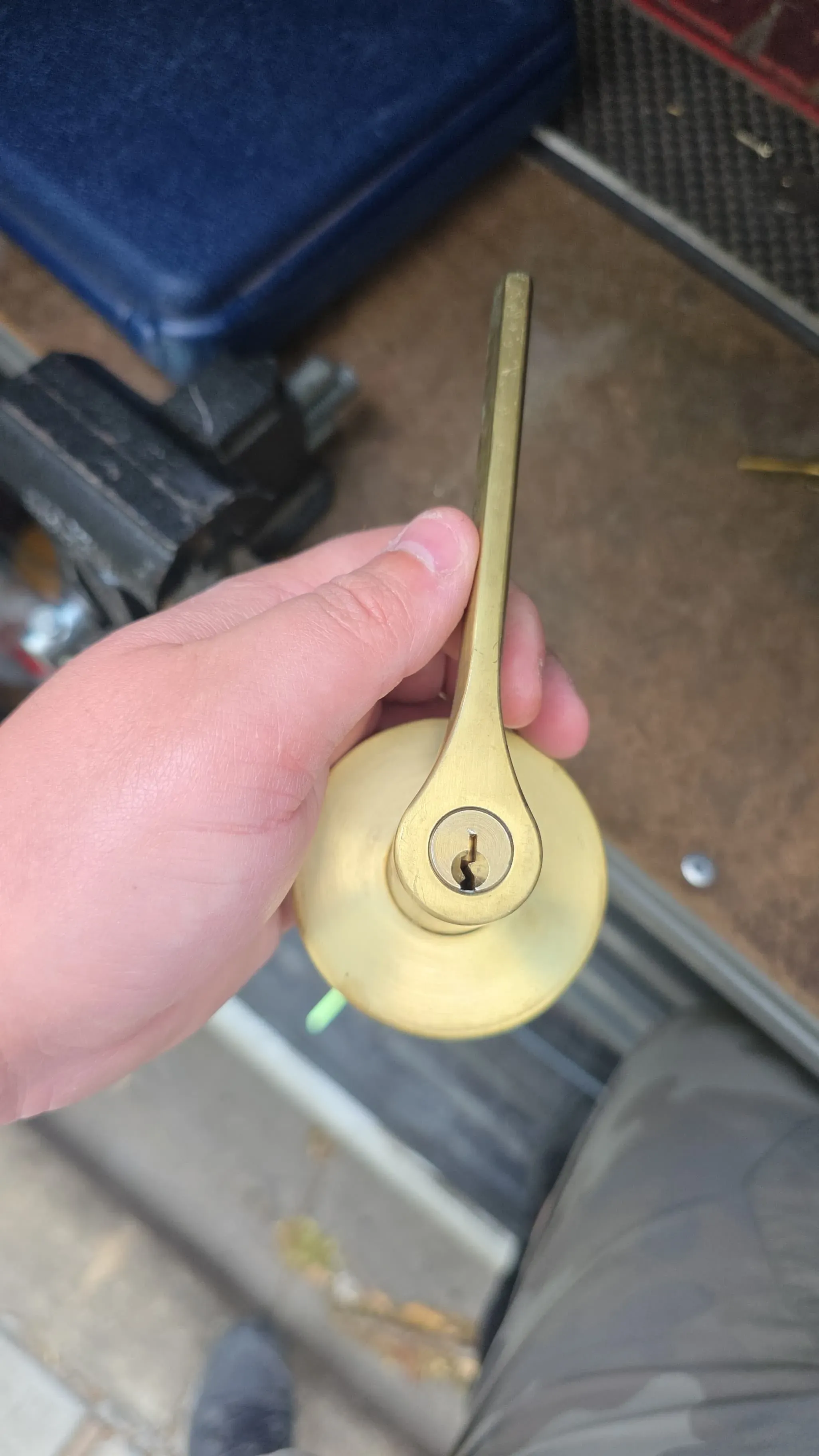 A technician's hand holding a removed brass lever lock cylinder for inspection