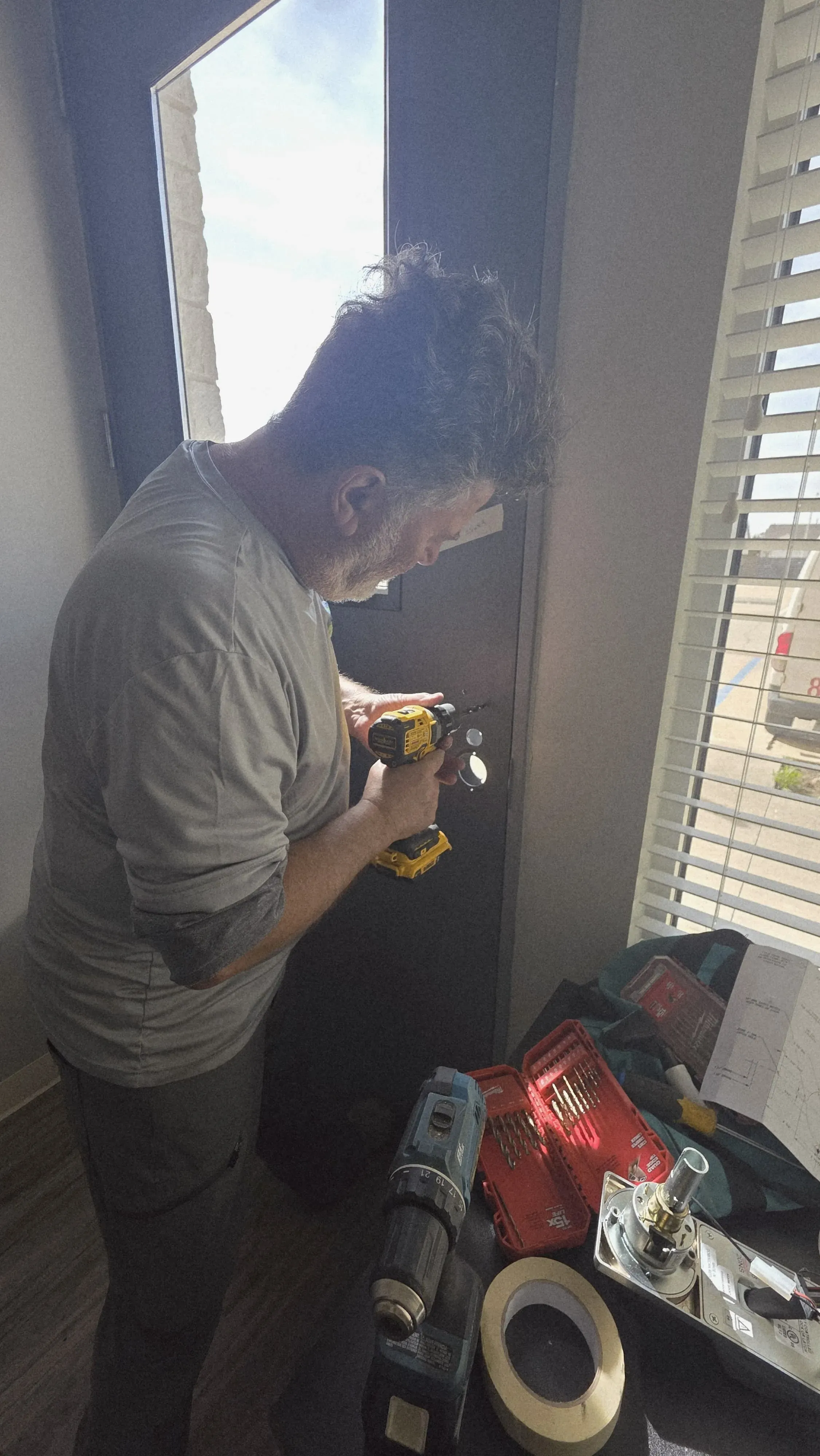 A Pros On Call technician drilling into a door frame to install reinforced hardware, tool tray in the foreground
