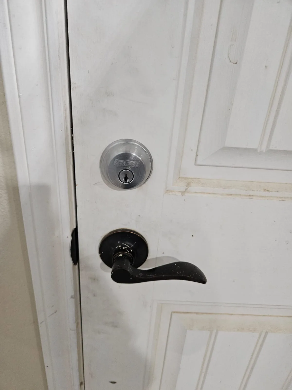 Schlage deadbolt and black lever installed on a white residential panel door by Pros On Call