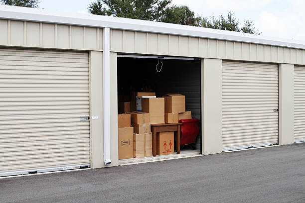 Warehouse building with self storage units. Self storage facility. Roll up doors on self storage facility. One door open with boxes, household goods and furniture in doorway. Several closed units also visible. For Commercial Garage Door Repair and Installation Plano TX choose Pros on Call